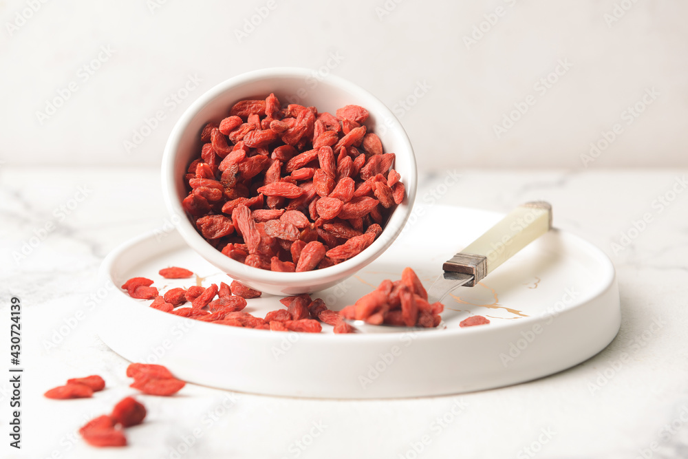 Bowl and spoon with dried goji berries on light background Bowl and spoon with dried goji berries on light background