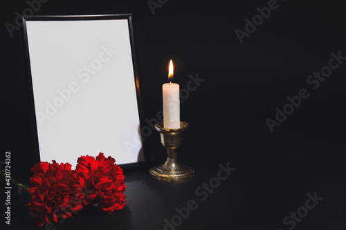 Photo frame with candle and carnation flowers on dark background photo