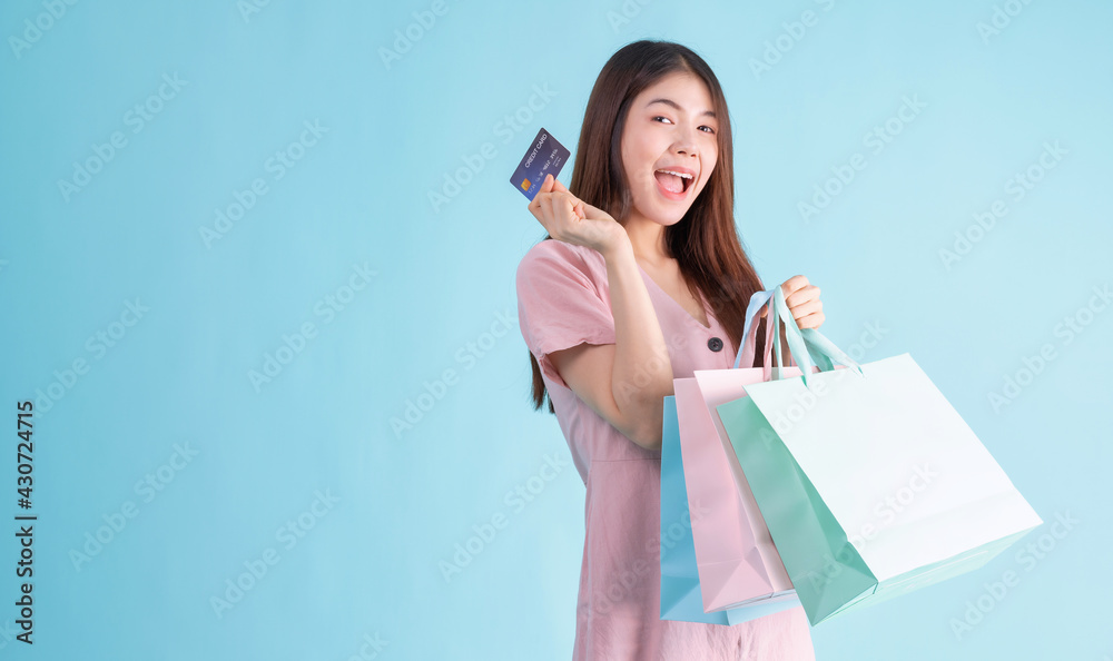 portrait of cheerful young brunette woman holding credit card and shopping bags over Blue background. shopaholic Concept portrait of cheerful young brunette woman holding credit card and shopping bags over Blue background. shopaholic Concept