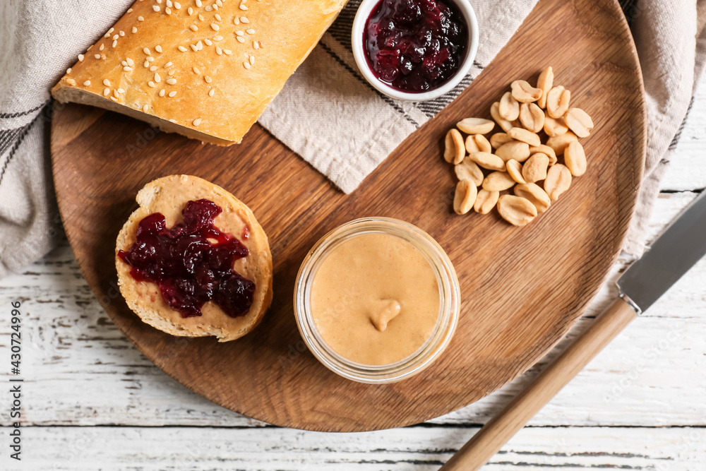 Fototapeta premium Jar with tasty peanut butter, bread and jam on light wooden background