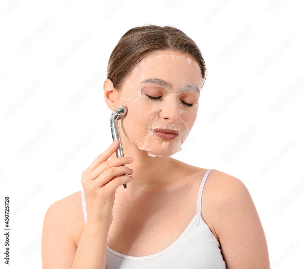 Beautiful young woman with sheet facial mask and massage tool on white background Beautiful young woman with sheet facial mask and massage tool on white background