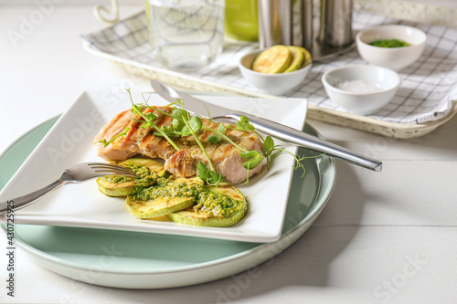 Plate with tasty grilled chicken meat, zucchini and pesto sauce on light wooden background, closeup