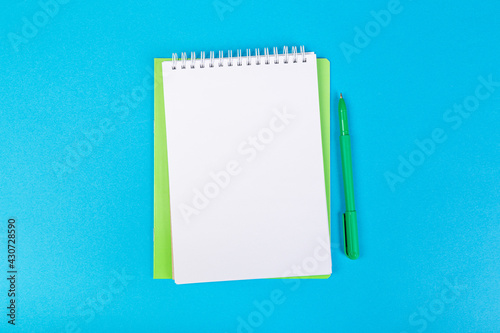 stack of school exercise books on blue background, spiral notepad with blank page and pen on table top view
