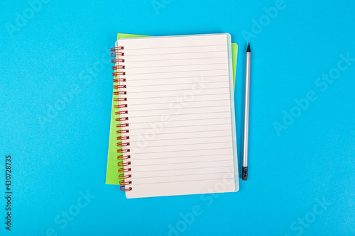 school notebooks on a blue background, spiral notepad with a blank page and a pencil on the table top view