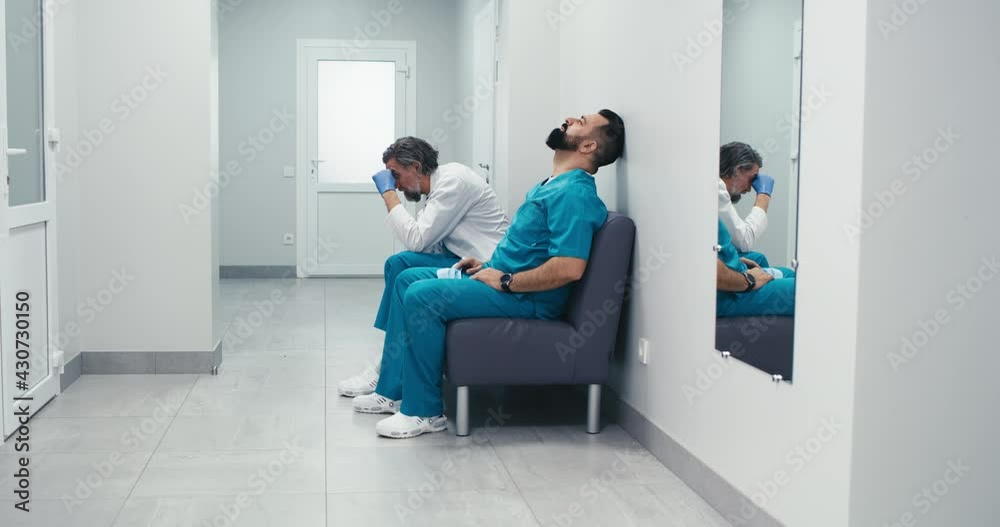 Stressed male doctors sitting on couch in clinic corridor Stressed male doctors sitting on couch in clinic corridor