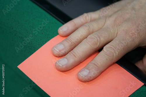 An adult male arbiter or voting participant takes out a paper red card from a cardholder. Warning  prohibition or disagreement with the decision. Close-up. Reportage