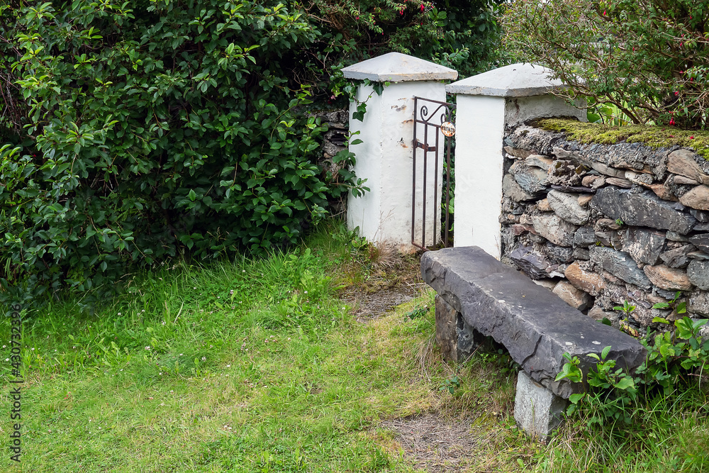 Solid stone bench by stone wall fence. Future proof design. House hold time made for future generation. Fine example of masonry craft. Old style furniture in a garden. Solid stone bench by stone wall fence. Future proof design. House hold time made for future generation. Fine example of masonry craft. Old style furniture in a garden.