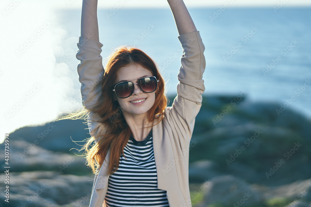 woman traveler in a sweater gesturing with her hands above her head near the sea in the mountains woman traveler in a sweater gesturing with her hands above her head near the sea in the mountains