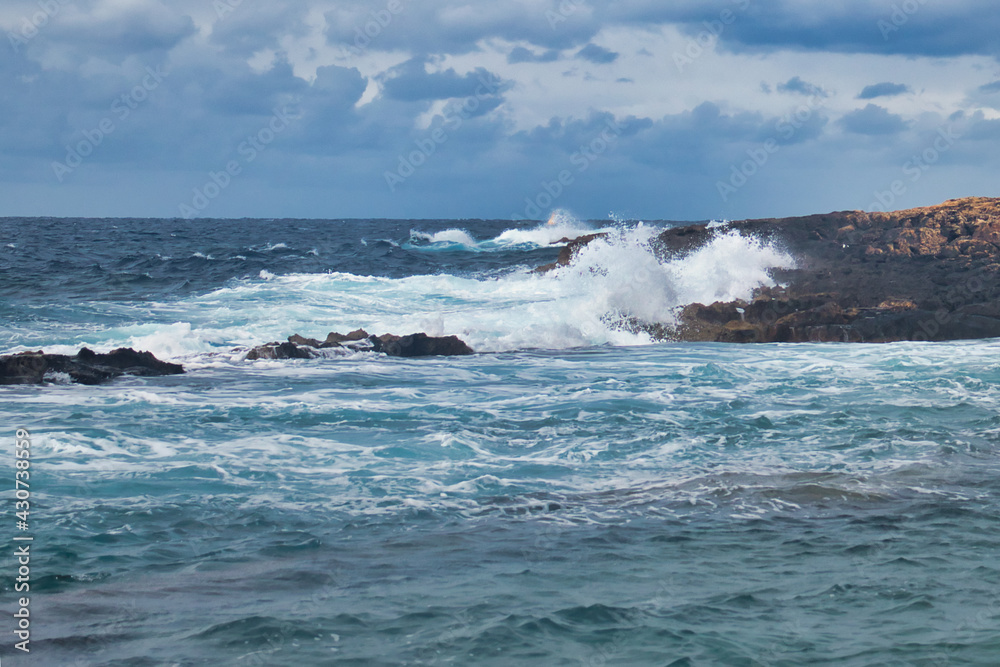 Blue water and sky on a stormy day in Qawra, Malta as waves crash against rocks.