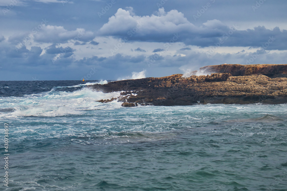 Water splashing in and on the rocks on a beach at Qawra, Malta on a cloudy day.