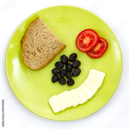 Plate of breakfast with cheese, tomato, olive and bread in big green plate, top view, isolated photo