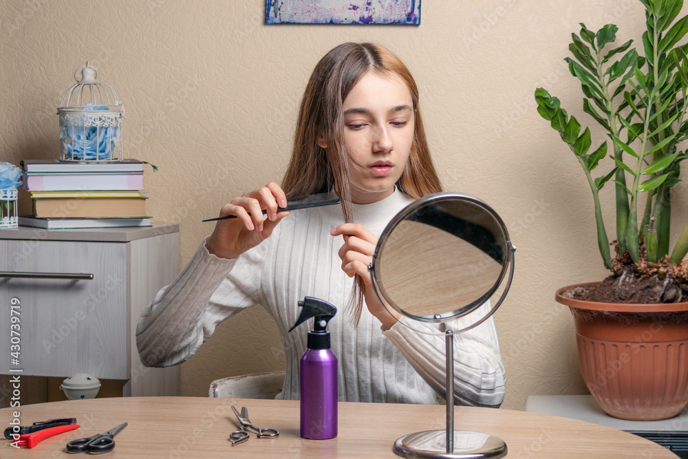 teenage girl with a comb in her hand looks in the mirror. beautiful teenage girl doing her hair in front of the mirror in her room. teenage girl with a comb in her hand looks in the mirror. beautiful teenage girl doing her hair in front of the mirror in her room.