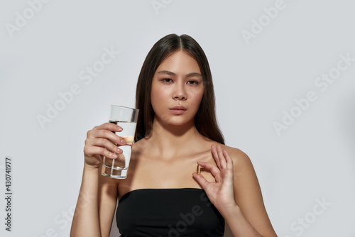 Young asian woman holding pill and glass of water