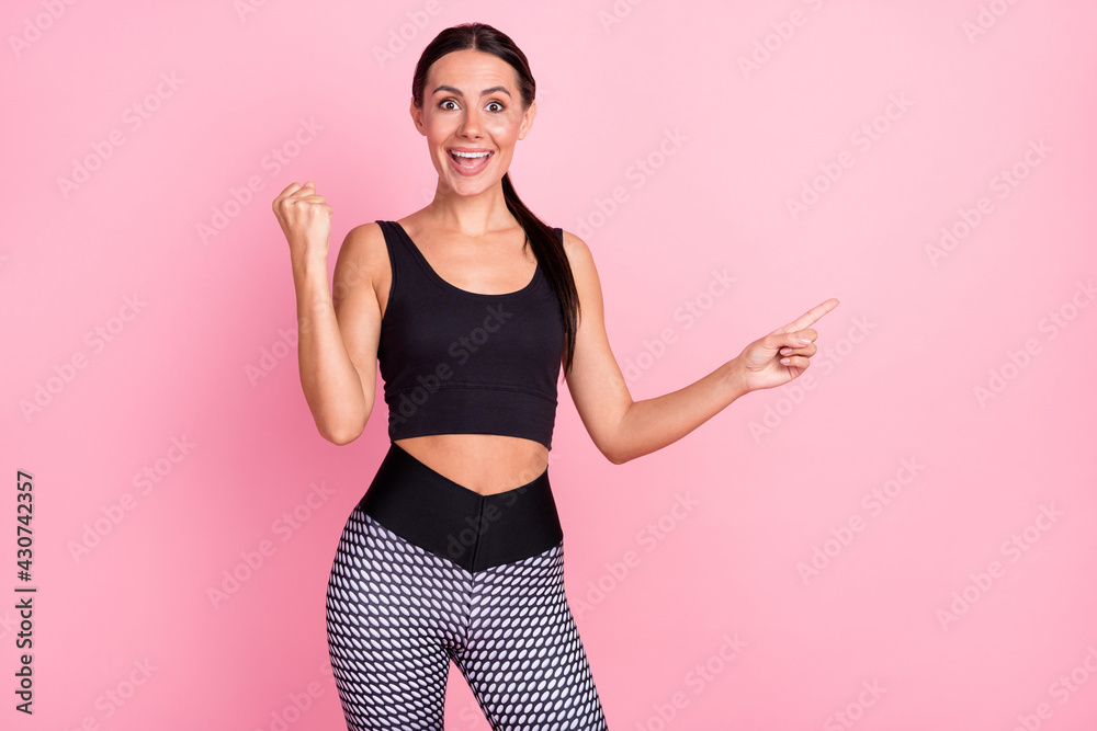 Photo of happy cheerful young woman point finger empty space raise fist win isolated on pink color background Photo of happy cheerful young woman point finger empty space raise fist win isolated on pink color background