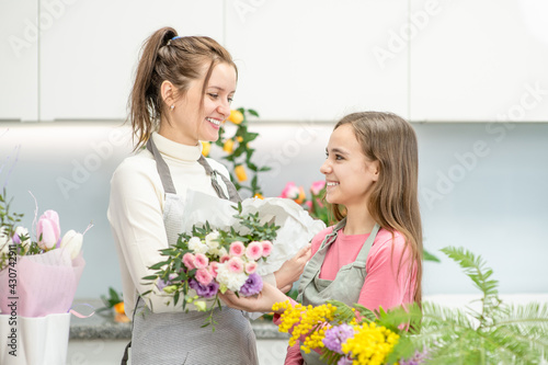 Woman teaches to young girl what arranging flower at flower shop