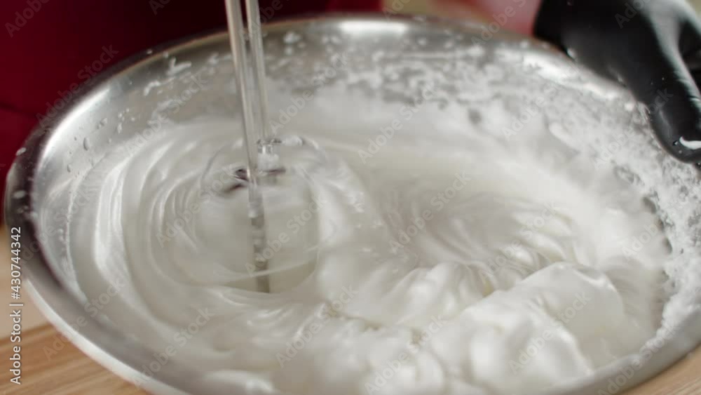 Male chef in black gloves whips egg whites with mixer in iron bowl in restaurant kitchen