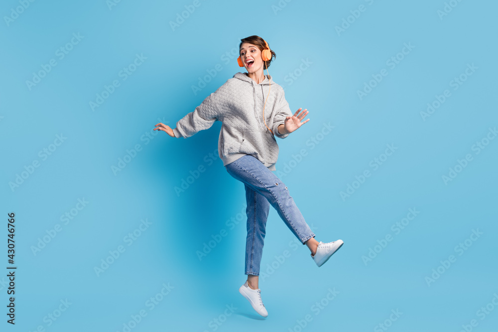 Full length photo portrait of girl kicking jumping up with headphones isolated on pastel blue colored background
