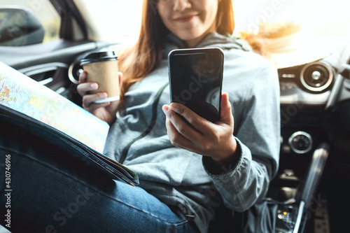 Closeup image of a woman holding and using mobile phone while riding the car