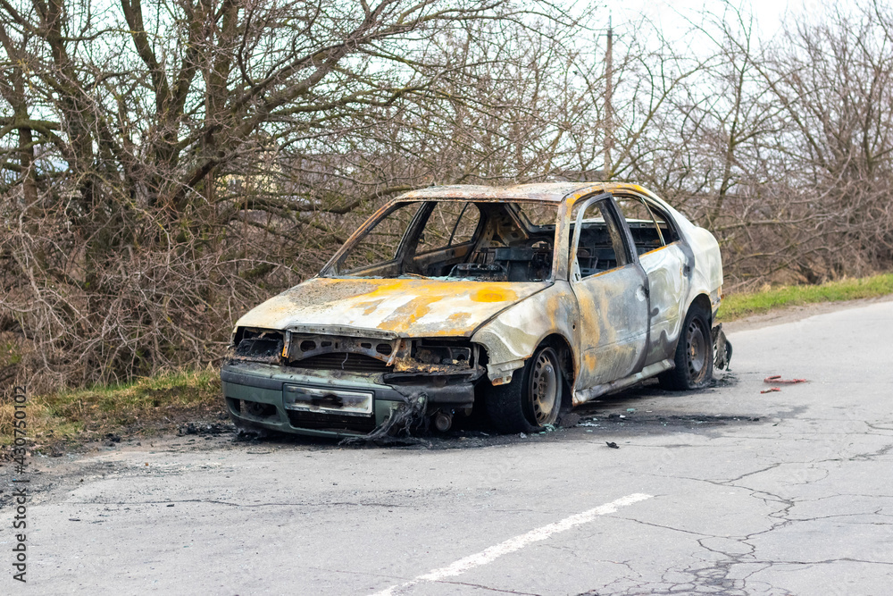 Burned car after an accident on the asphalt road. Front view. Arson of a car, criminal showdowns Burned car after an accident on the asphalt road. Front view. Arson of a car, criminal showdowns