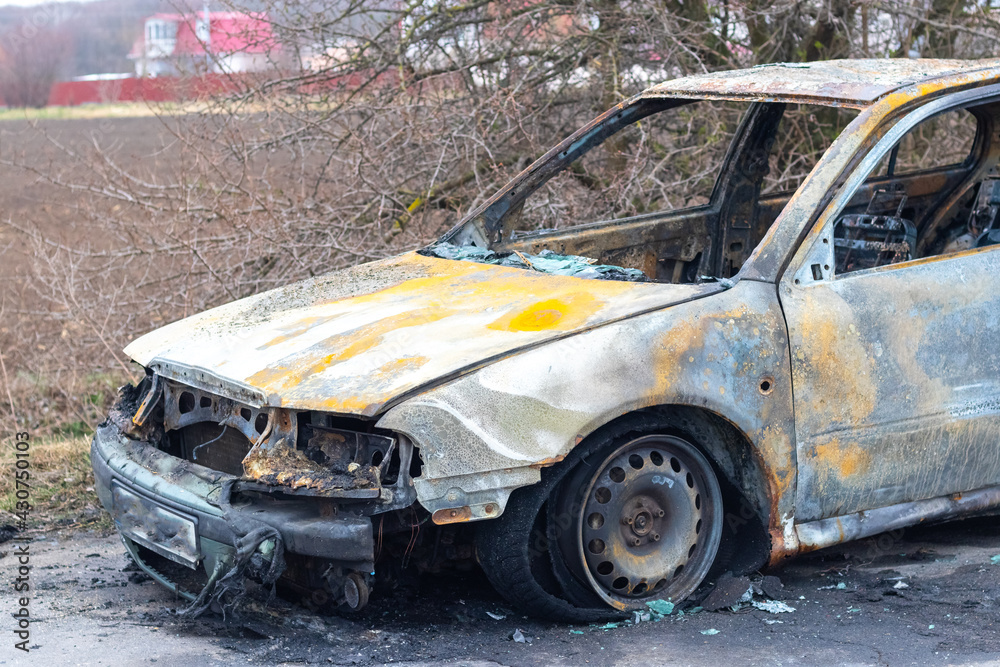 Burned car after an accident on the asphalt road. Close-up, fragment. Arson of a car, criminal showdowns Burned car after an accident on the asphalt road. Close-up, fragment. Arson of a car, criminal showdowns