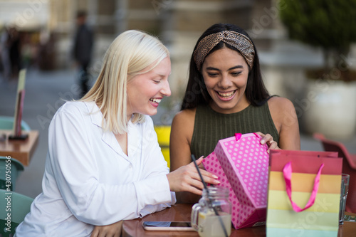 Two women in café sitting and looking in shopping bag.