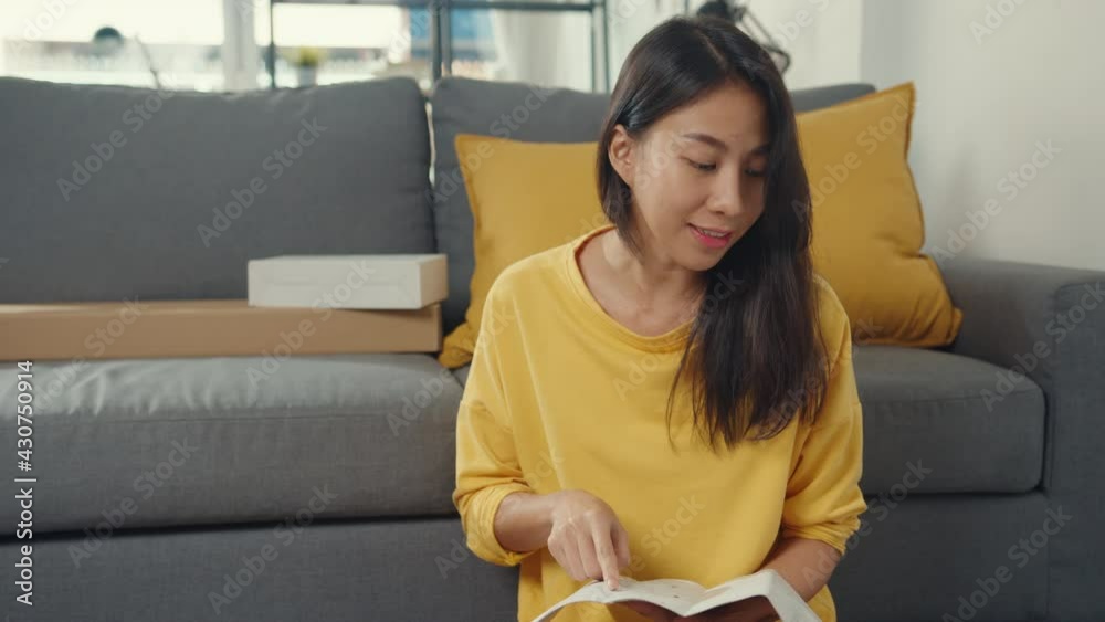 Happy asian young woman unpacking box and reading the instructions to assemble new furniture decorate house build table with carton box in living room at home.