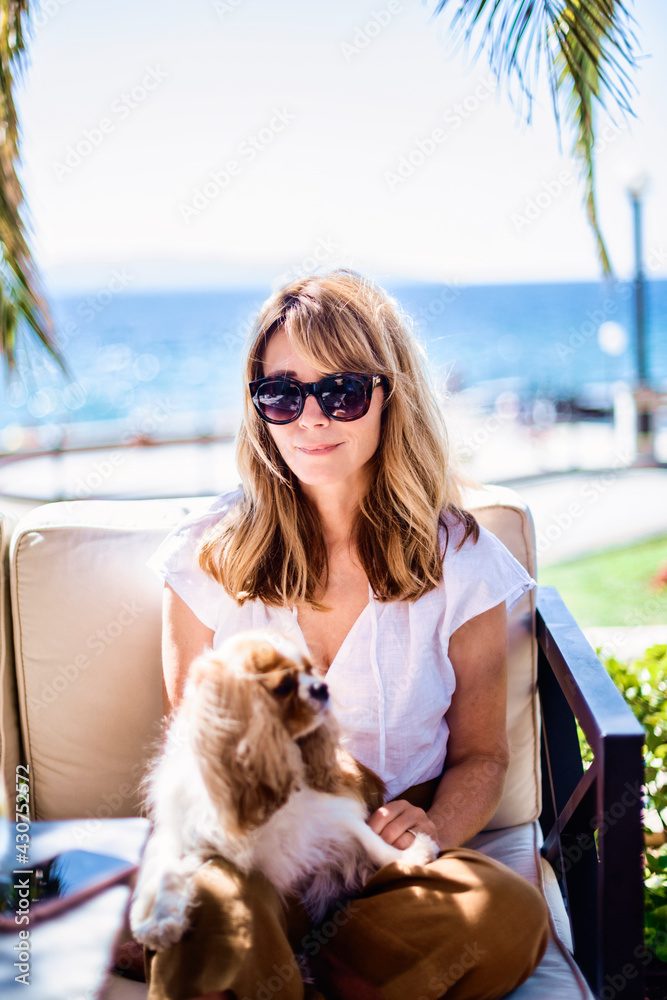 Middle aged woman relaxing in the chair with her cute puppy with background the sea Middle aged woman relaxing in the chair with her cute puppy with background the sea