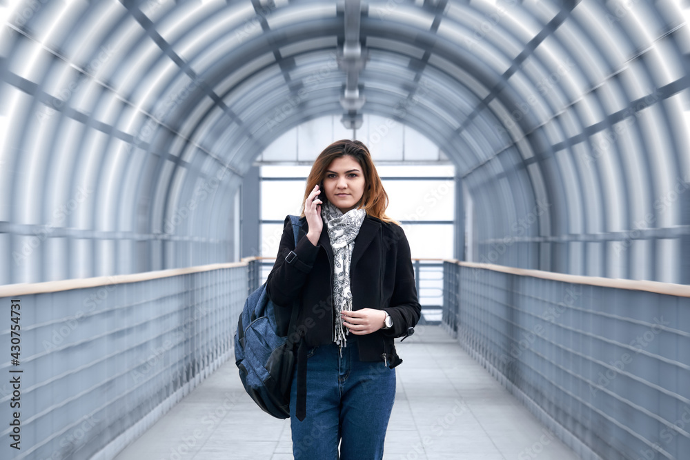 young woman is walking rapidly along the covered pedestrian overpass, talking on the phone young woman is walking rapidly along the covered pedestrian overpass, talking on the phone