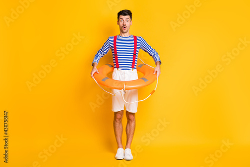 Full length photo of amazed brunette man hold lifeguard circle wear summer sailor outfit isolated on yellow color background photo