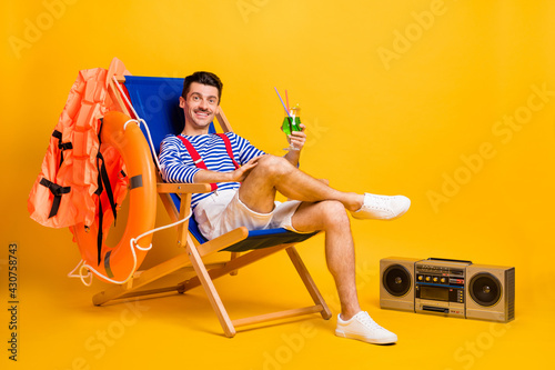 Full size photo of brown haired man hold cocktail sit chair beach lifeguard wear sailor outfit isolated on yellow color background