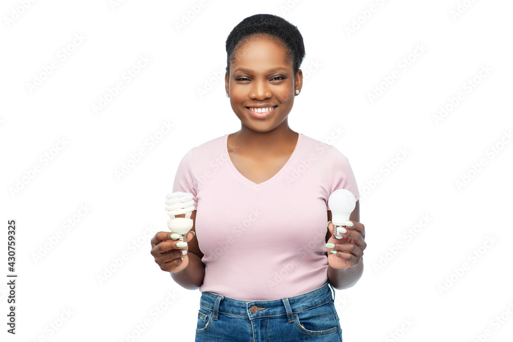 eco living, inspiration and sustainability concept - portrait of happy smiling young african american woman comparing lighting bulbs over white background eco living, inspiration and sustainability concept - portrait of happy smiling young african american woman comparing lighting bulbs over white background