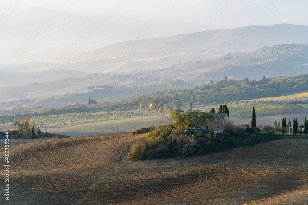 Fototapeta premium A stunning landscape view on an autumn morning of the hills of Tuscany with ploughed and green grass covered with beautiful undulating fields. The sunlight covering the meadows and fields makes