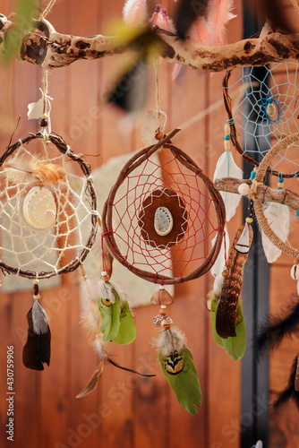 Round handmade dream catcher with seashell in the center and green feathers on wooden background