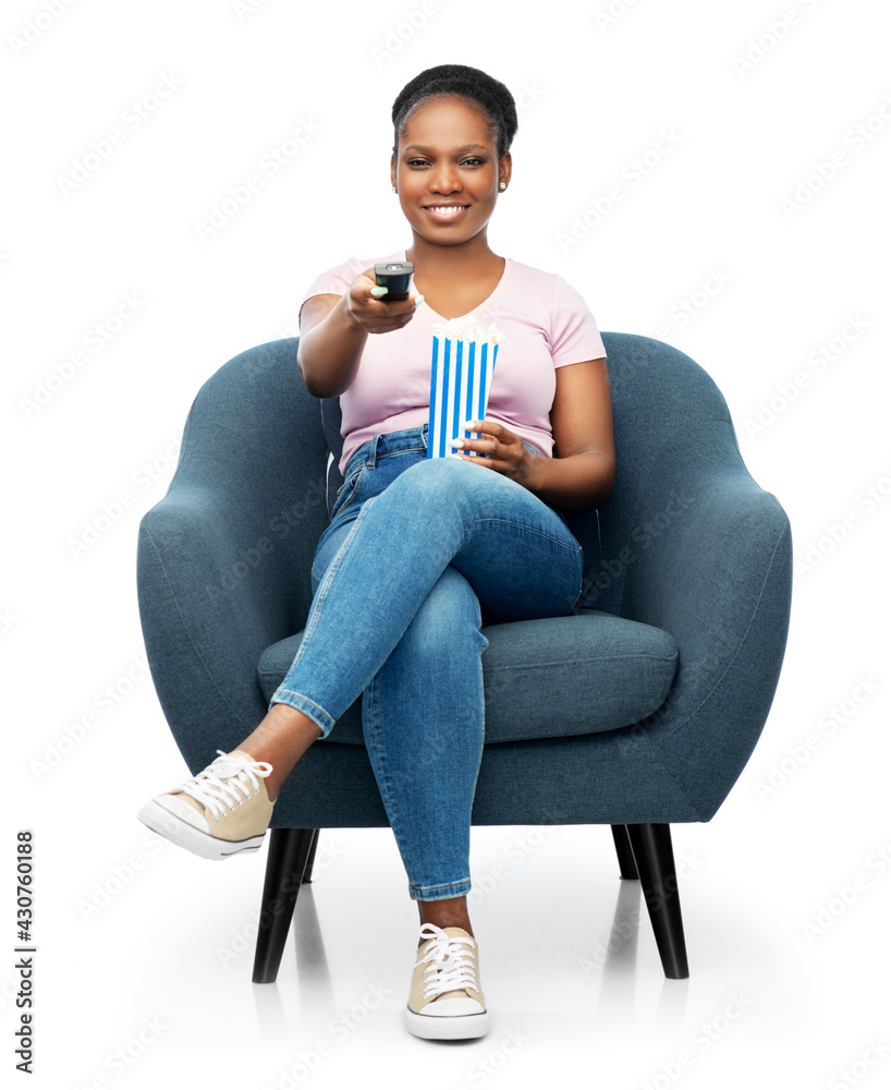 © Syda Productions - fast food and people concept - happy smiling african american woman eating popcorn from striped bucket sitting in modern armchair over white background