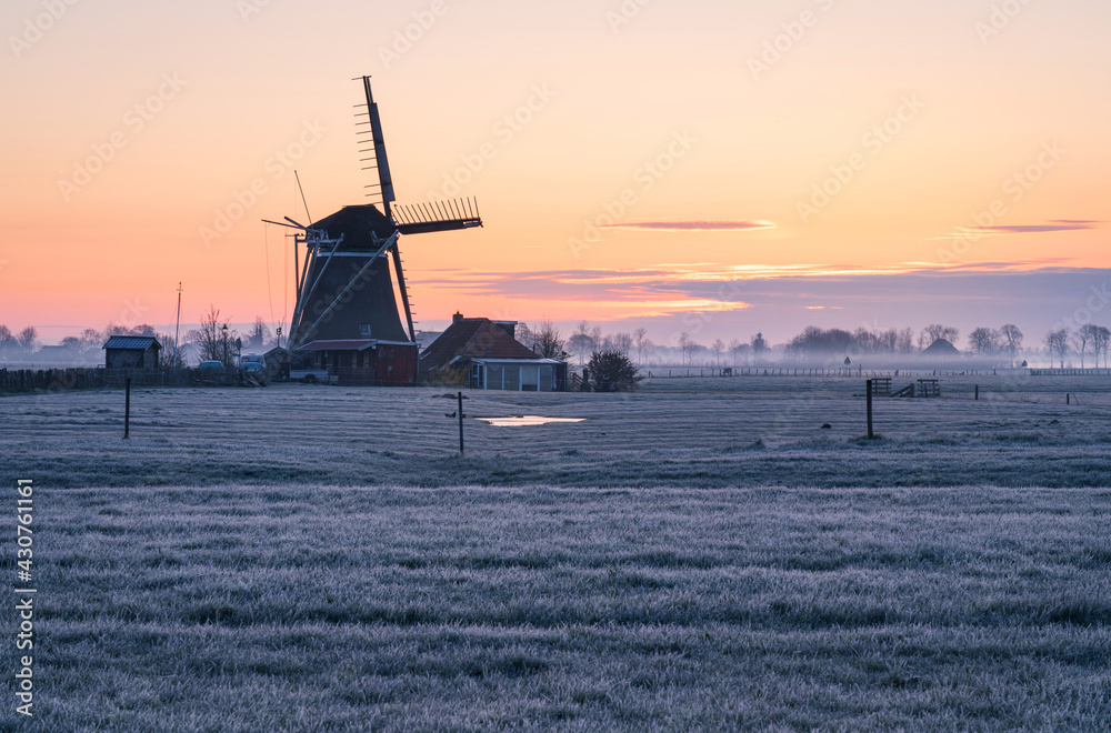 Foggy, spring sunrise in the Dutch countryside near a windmill.