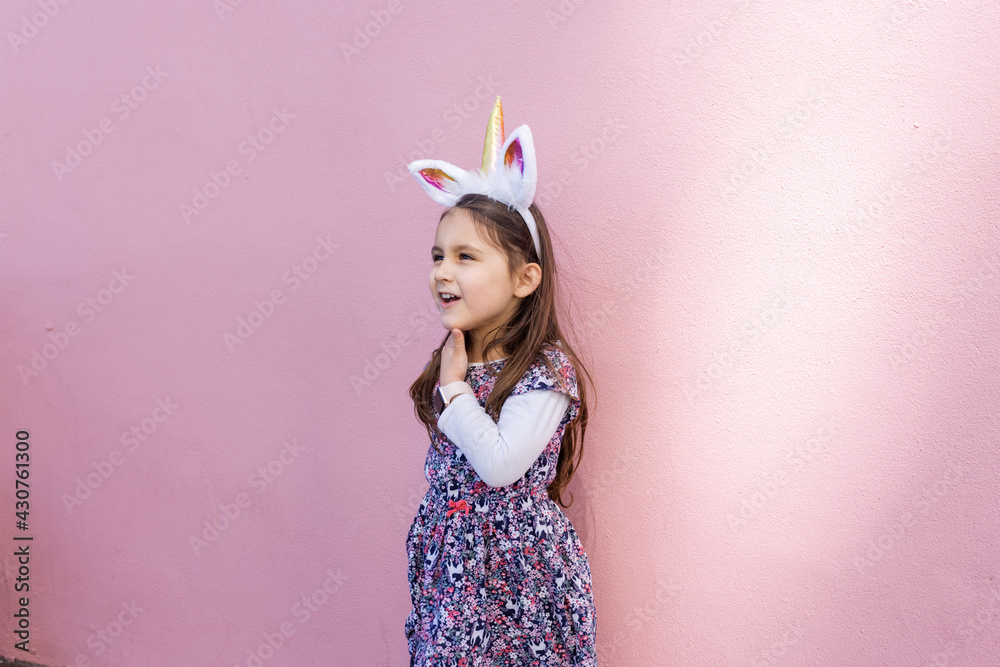 Adorable little girl wearing a unicorn headband with pink background