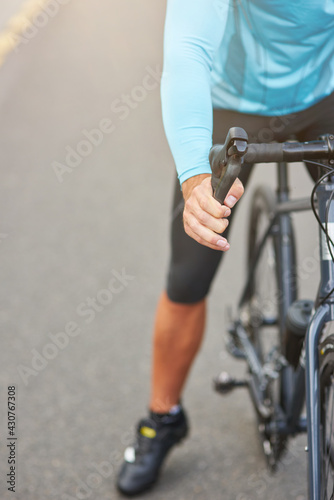 Cropped shot of professional male cyclist wearing suit having a rest, standing with his bike on the road outdoors