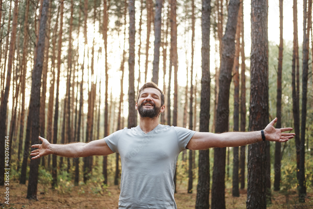 happy Caucasian male in the forest. He spread his arms and closed his eyes. Wellness concept and holistic health practices