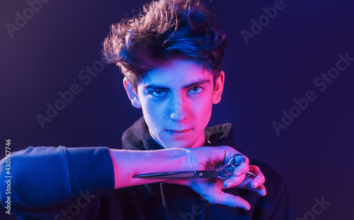 Young barber with work equipment standing in the studio with neon lighting