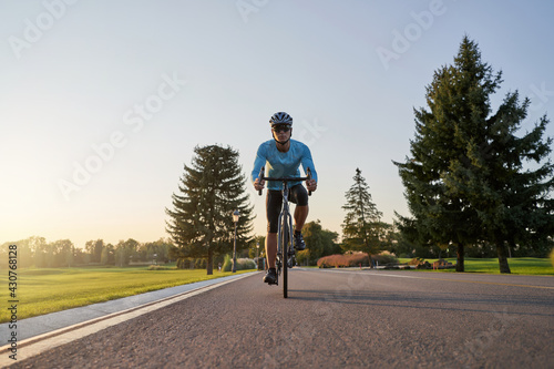 Fototapeta Naklejka Na Ścianę i Meble -  Full length shot of professional male cyclist in sportswear and protective helmet training in the park at sunset