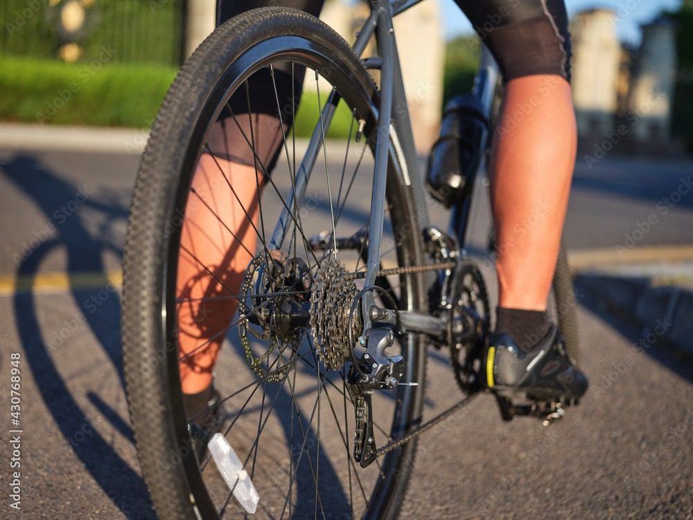 Fototapeta premium Close up view on wheel and chain of road bike. Professional cyclist riding a bicycle in park on a sunny day