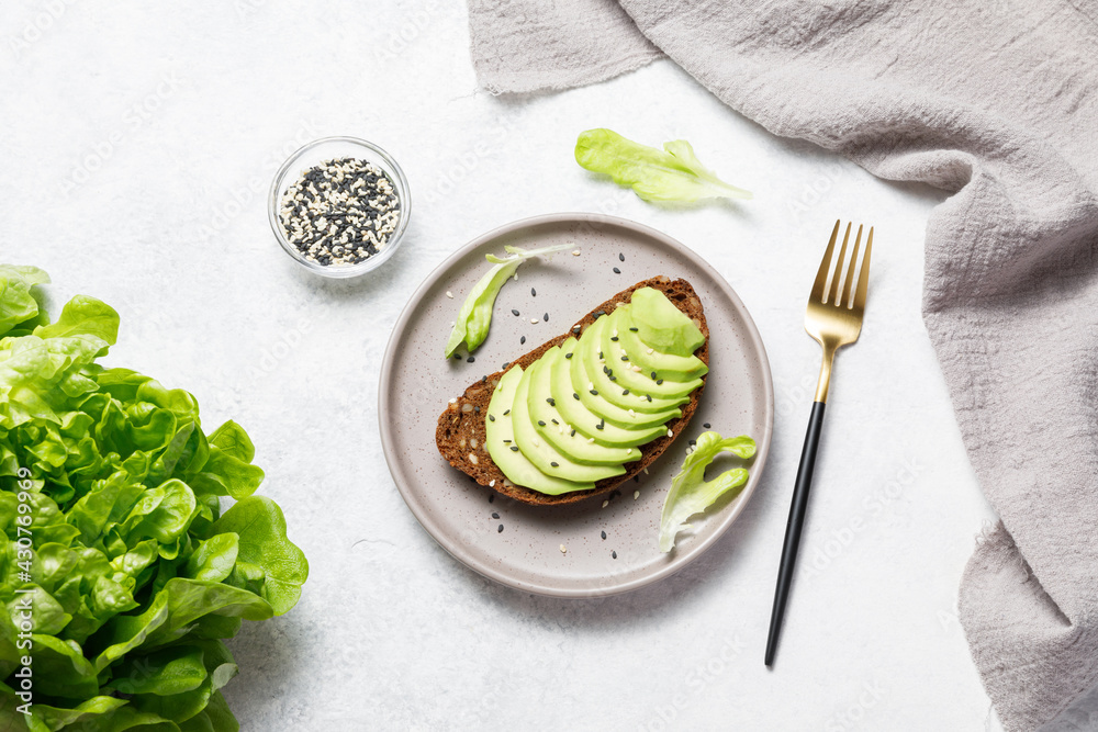 Whole grain rye bread toast with sliced avocado on white stone table background. Healthy avocado open sandwich for breakfast or lunch. Flat lay, top view