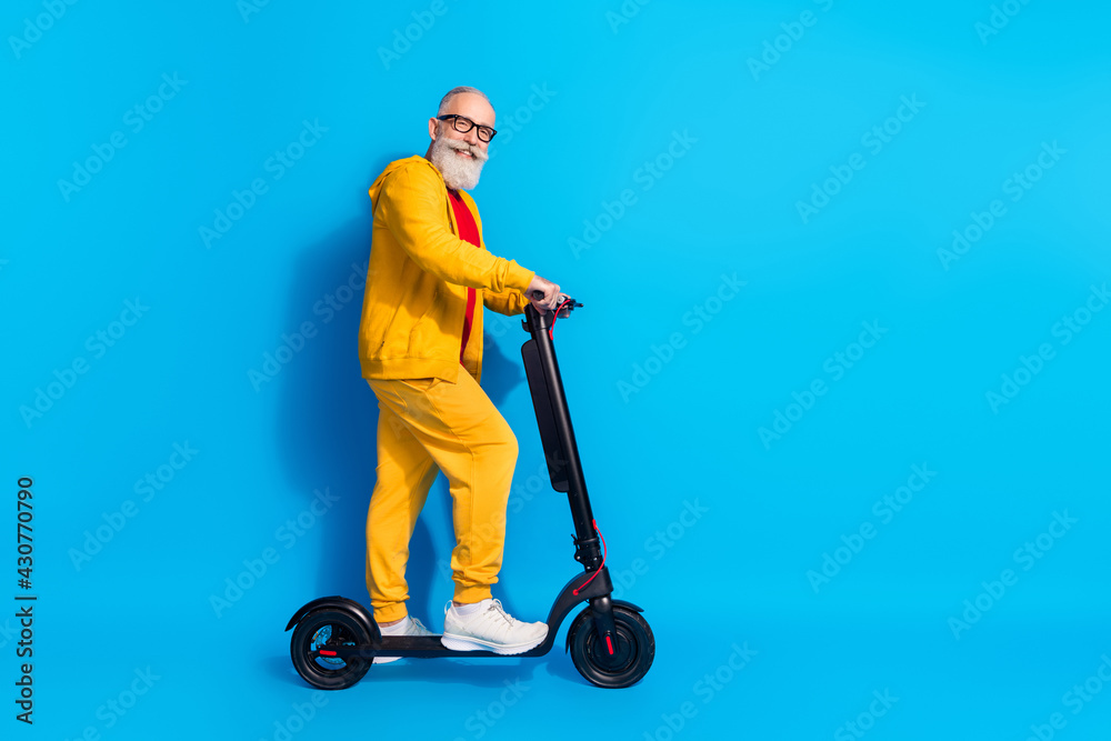 Full length profile photo of candid friendly aged man stand on vehicle look camera isolated on blue color background Full length profile photo of candid friendly aged man stand on vehicle look camera isolated on blue color background