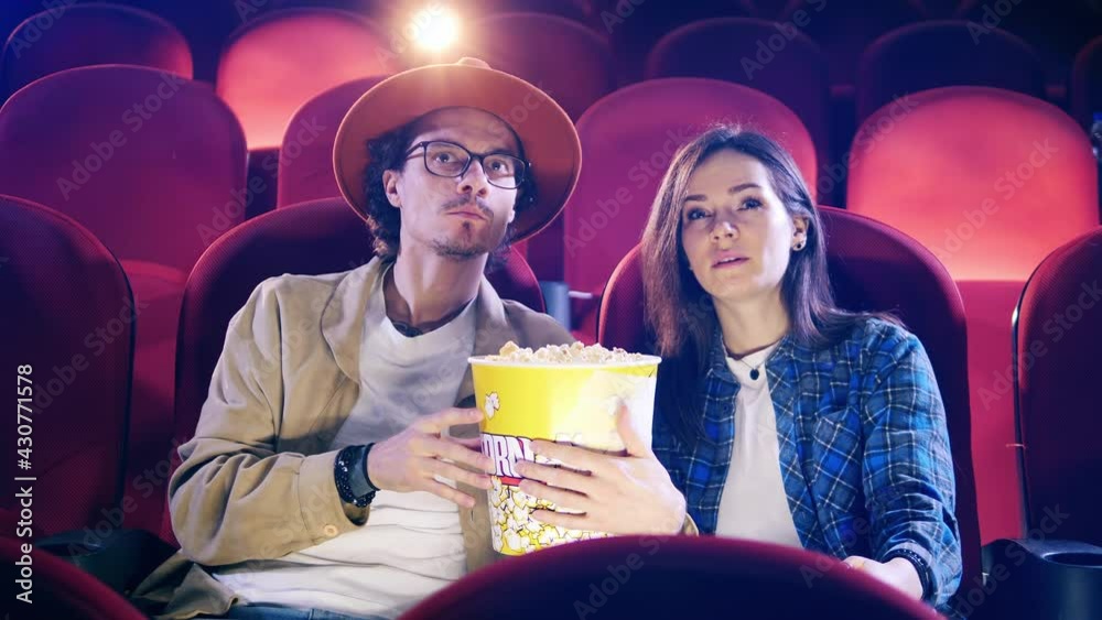 A man and a woman are eating popcorn while watching a movie A man and a woman are eating popcorn while watching a movie
