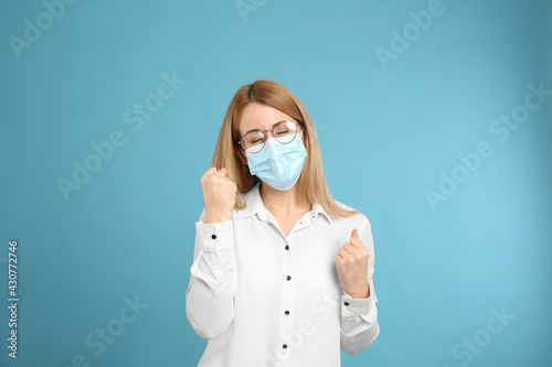 Emotional woman with protective mask on light blue background. Strong immunity concept