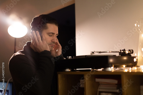 Young unshaven handsome millennial guy listens enjoys to music with headphones closed eyes. audiophile enjoying sound of retro vinyl records on analog turntable. Musical Hobby Concept