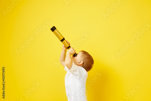 Side view of a child looking through a telescope on a yellow background. The concept of travel, pirates and adventures, active lifestyle, striving for the goal