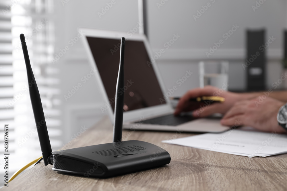 Foto de Man working with laptop in office, focus on connected router.  Wireless internet communication do Stock | Adobe Stock