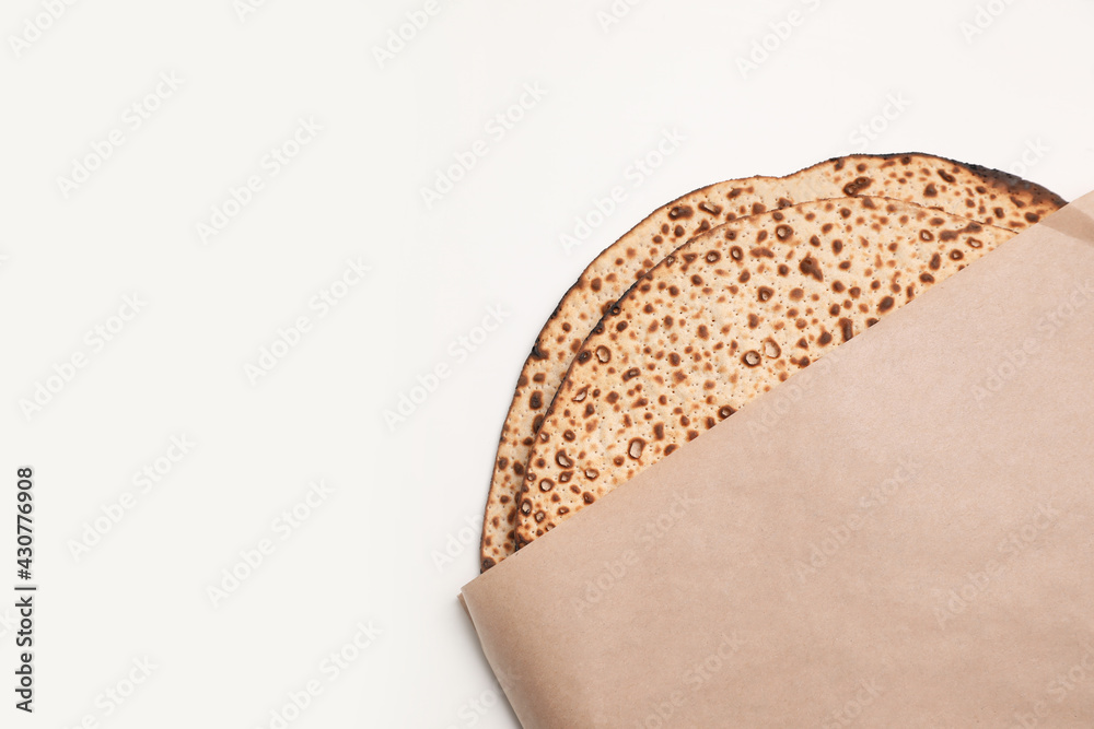 Fototapeta premium Tasty matzos wrapped with paper on white background, top view. Passover (Pesach) celebration
