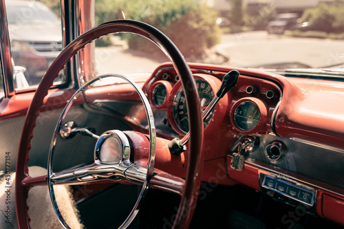 Steering wheel and red dashboard of classic car on sunny day. Interior of vintage automobile, retro style concept © Josu Ozkaritz